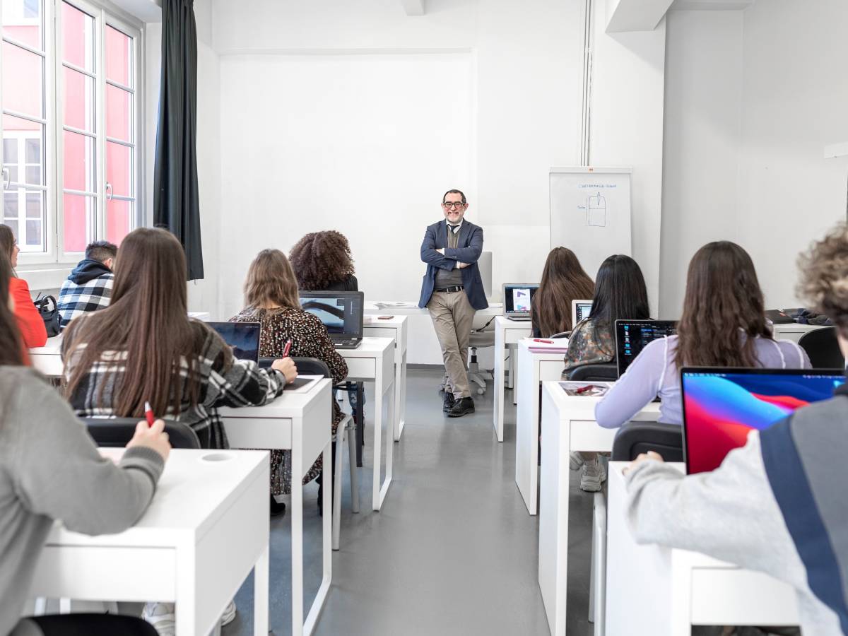 A class of students at their desks facing a smiling teacher