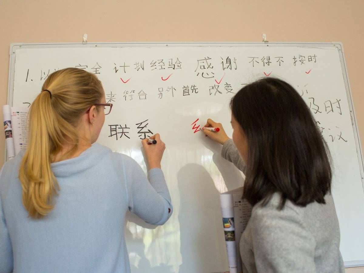 A CLI student and her teacher write Chinese characters side by side on a whiteboard during a one-on-one lesson.