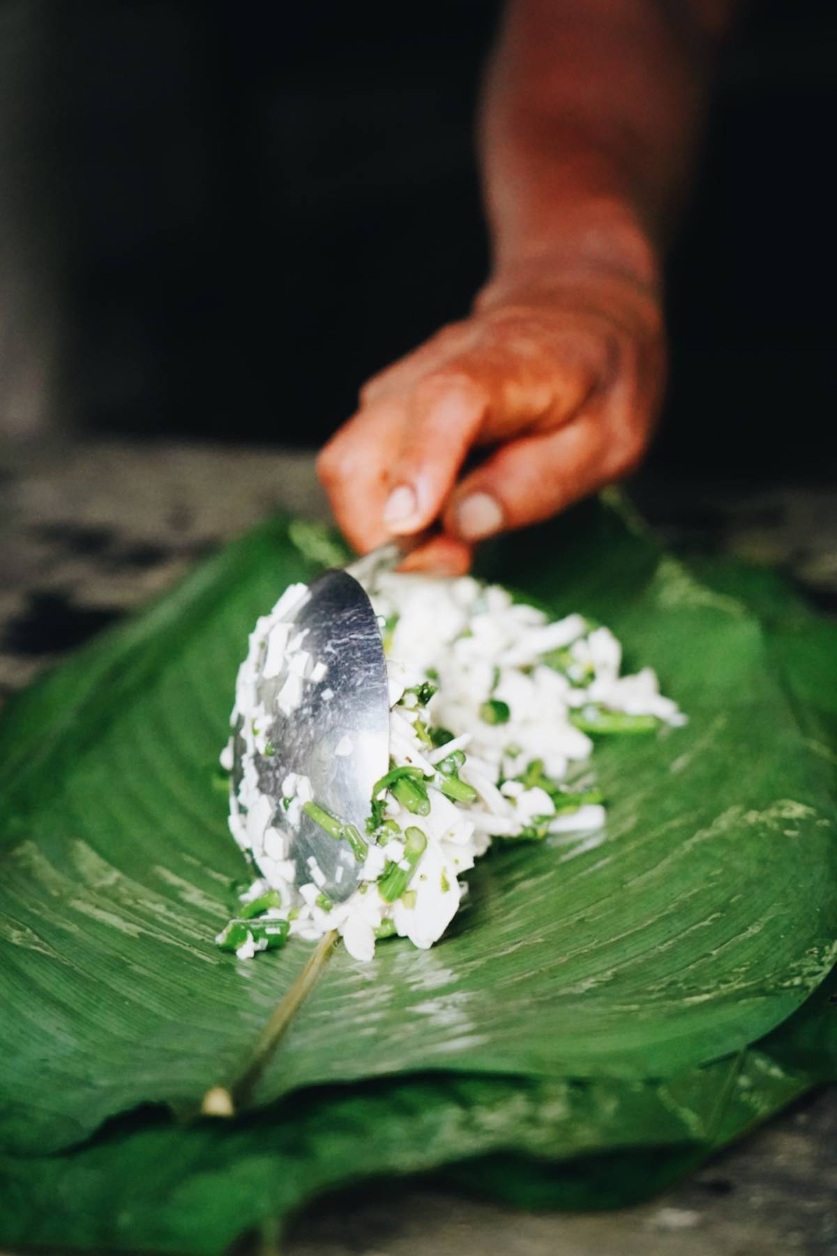 A close up of someone spooning food onto a large leaf.