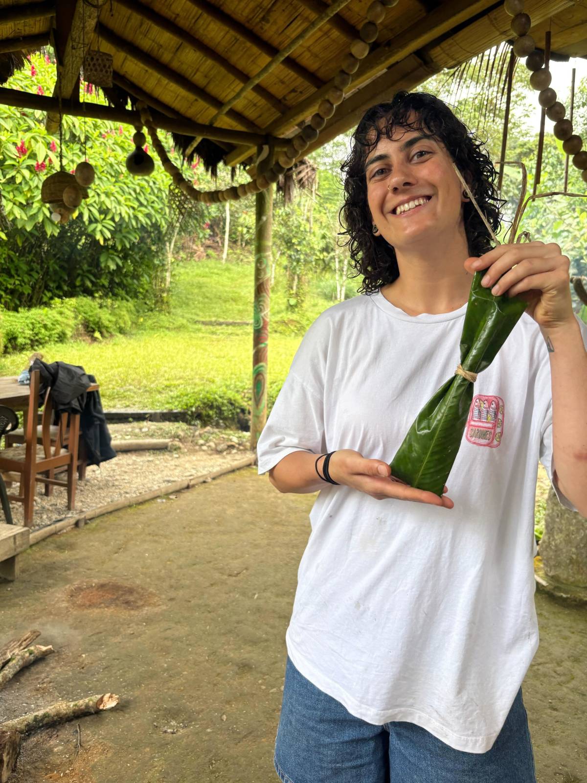 A girl smiles at camera while showing food wrapped in leaves.