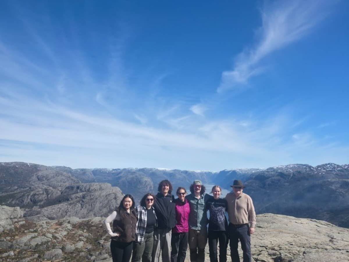 a group of 7 people stand on a mountain with blue skies in the background