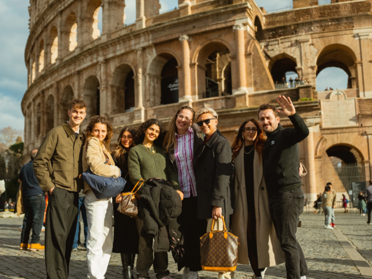 A group of EF Gap Year students smiling and posing together in front of the Colosseum in Rome on a sunny day, enjoying their study abroad experience.