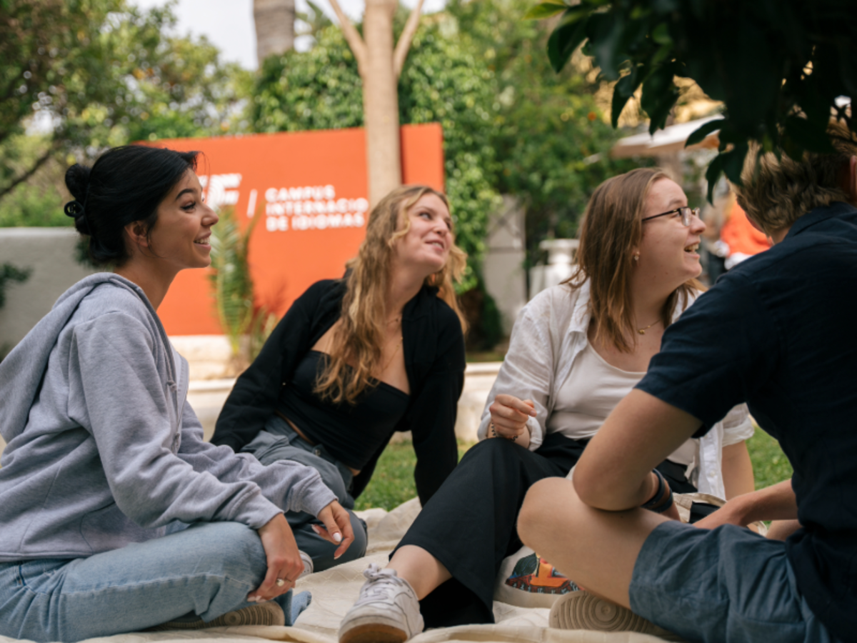A group of EF students sit outdoors on campus in Malaga, smiling and talking together.