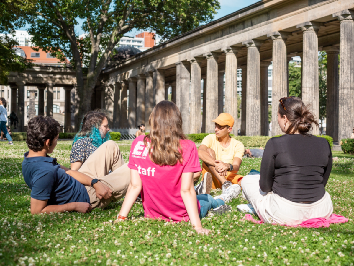 A group of EF students sits on the grass with an EF staff member in Berlin, with historic stone columns in the background.