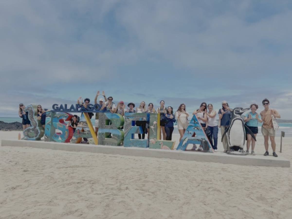 a group of people posing for a photo in front of a sign that reads Galápagos and Isabela
