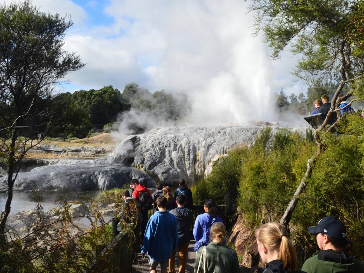 A group of students walking in nature with smoke billowing from a natural thermal area