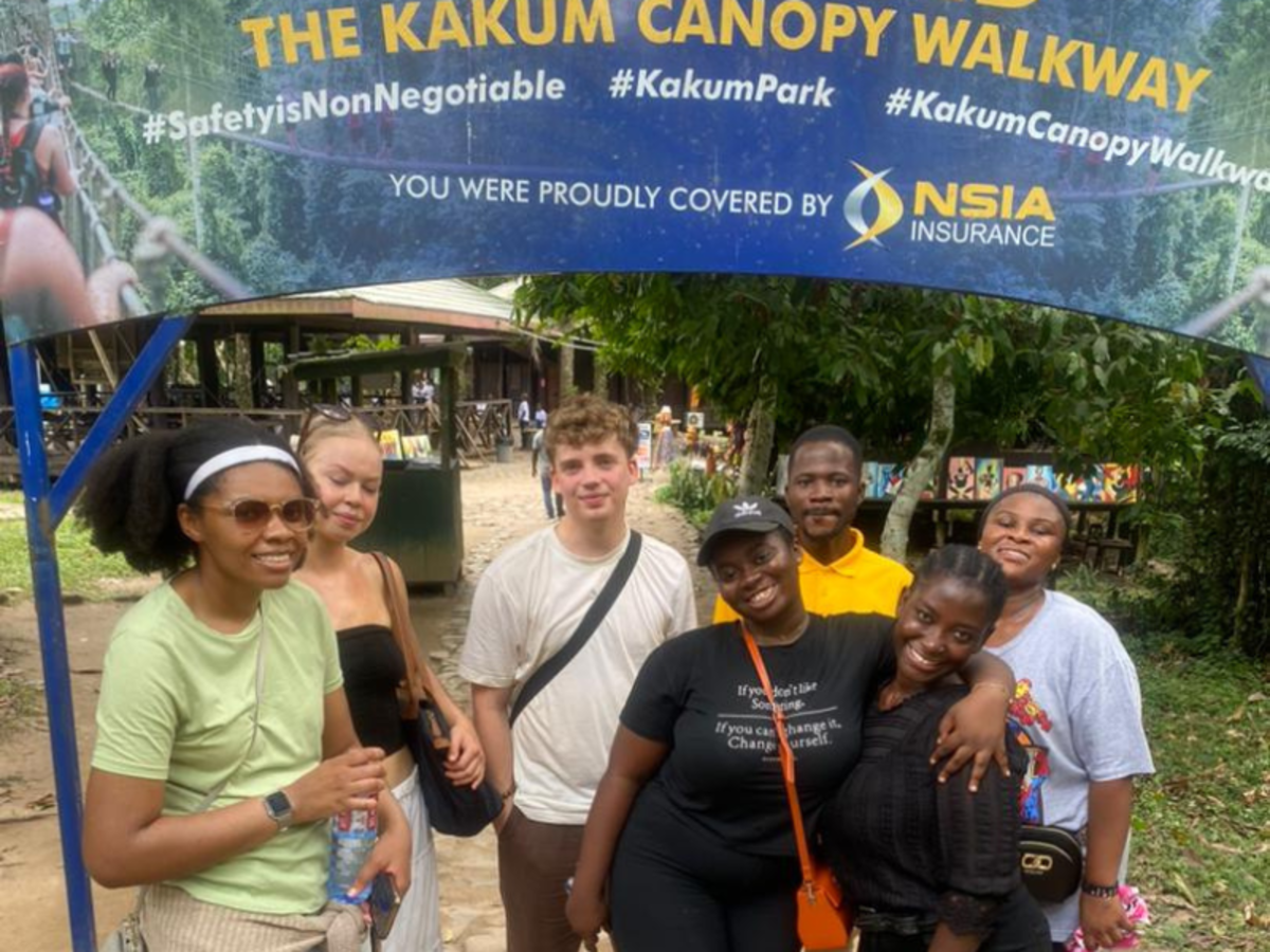 A group of volunteers and staff stand smiling in front of a sign that reads 'The Kakum Canopy Walkway'