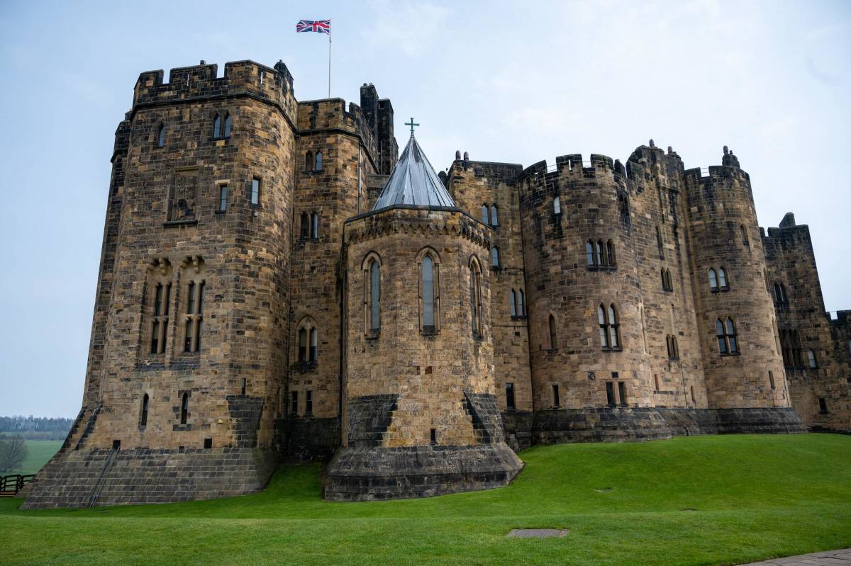 A large yellow stone building rises out of a lush green landscape, with a Union Jack flying above it.