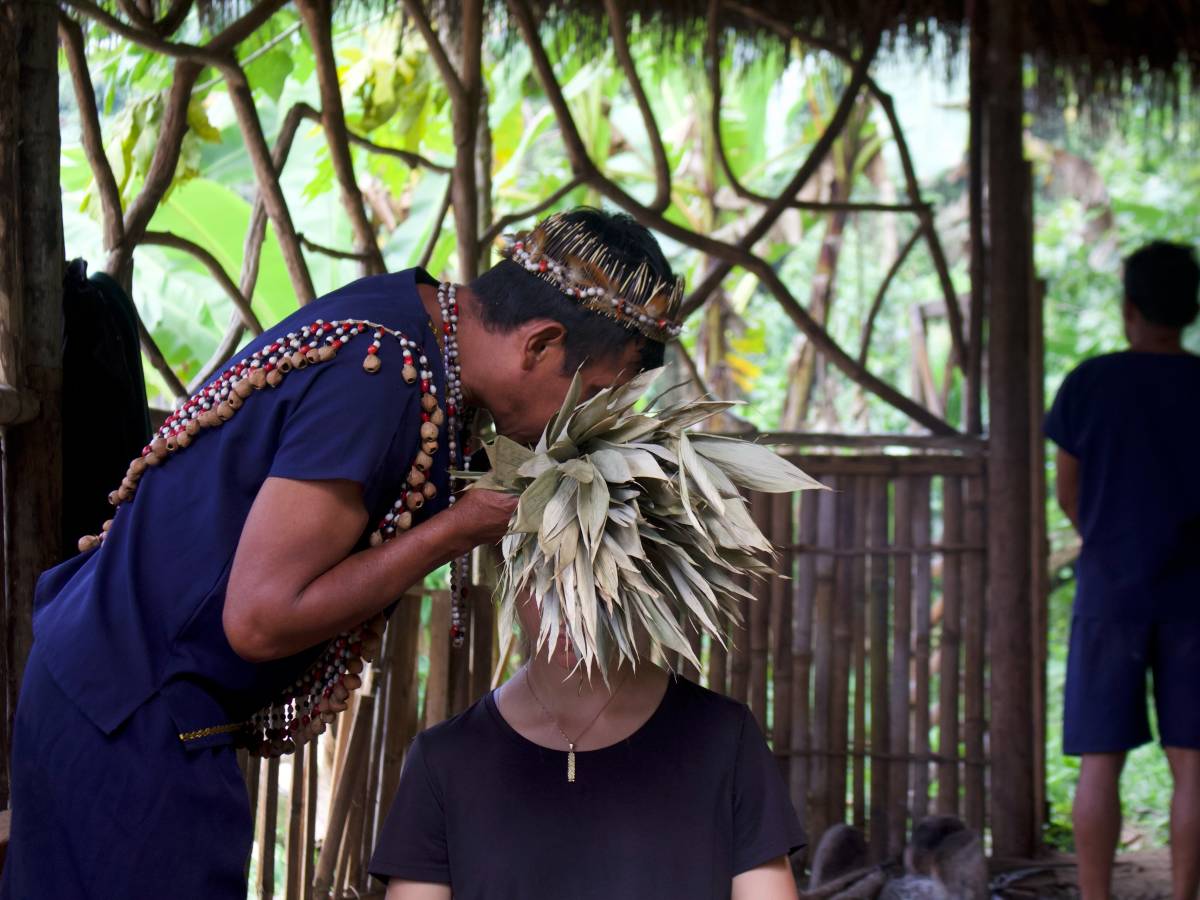 A man in traditional clothes blows on the head of an person.