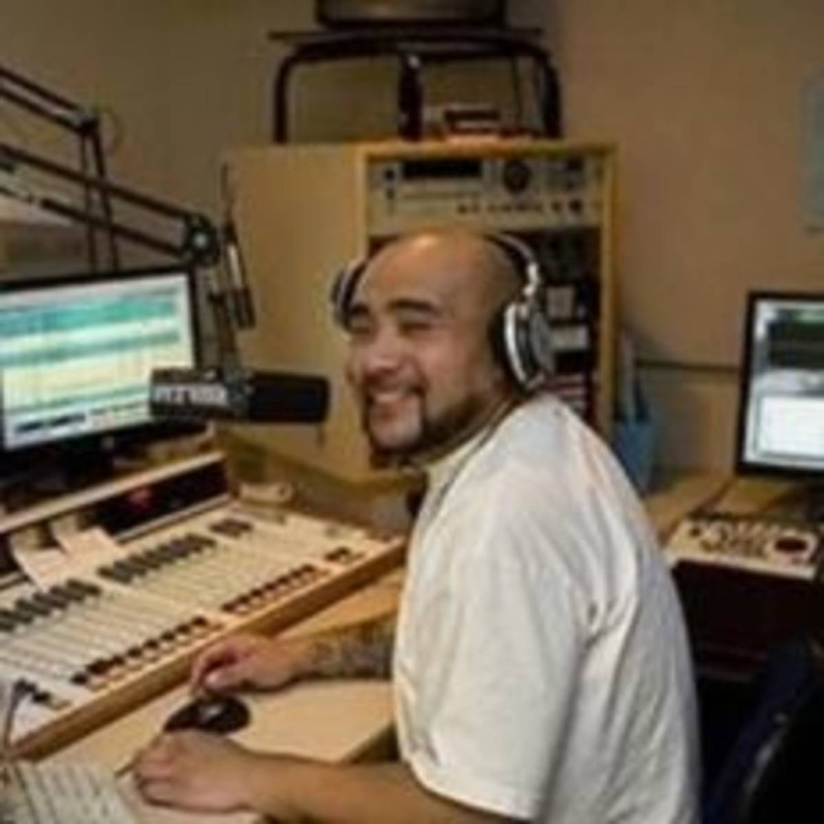 A man sitting while smiling at a desk in front of a radio, listening intently.