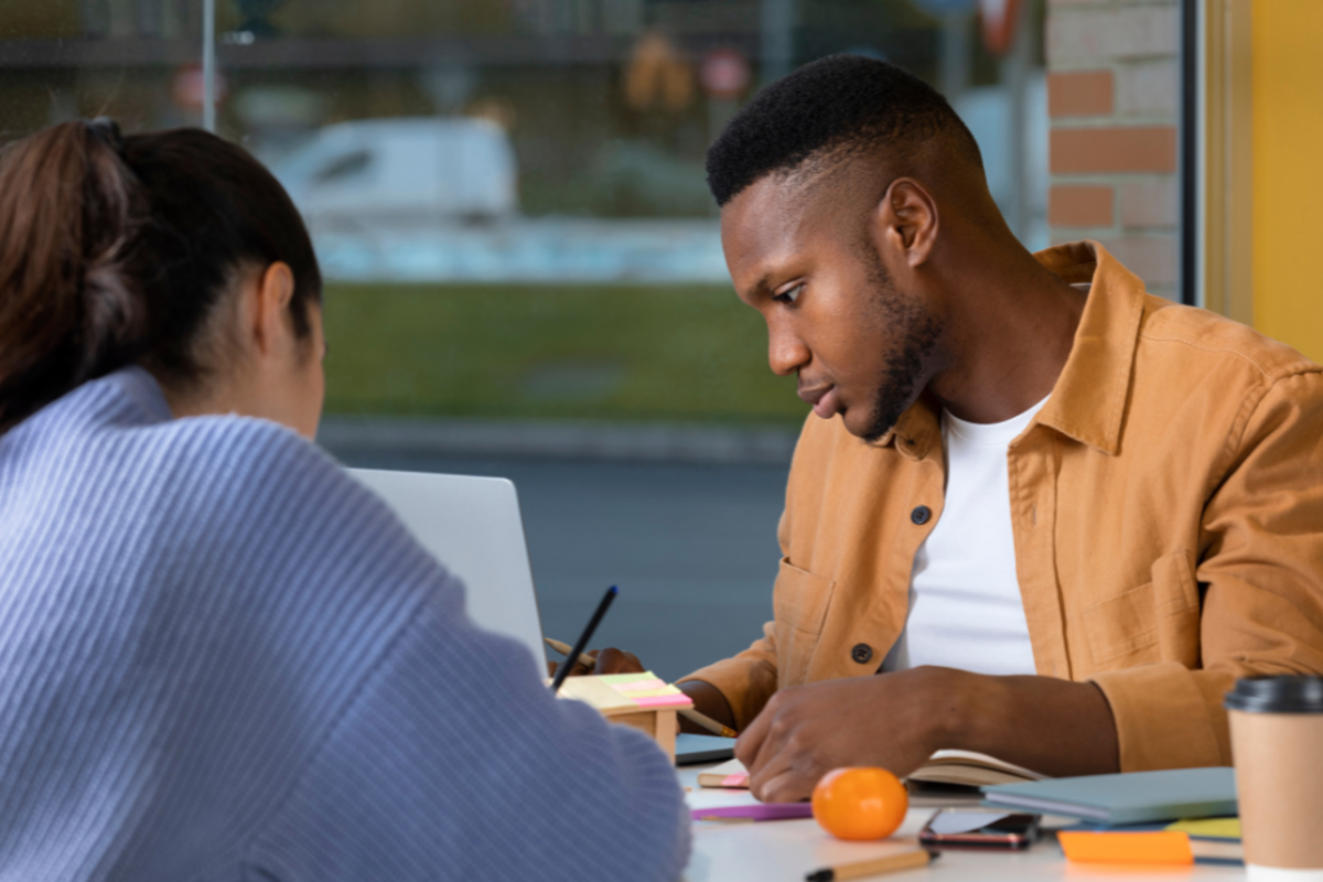 a man working alongside another person at a table with a laptop