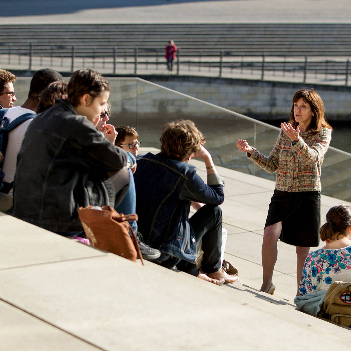 A professor lectures her class outdoors on concrete steps.