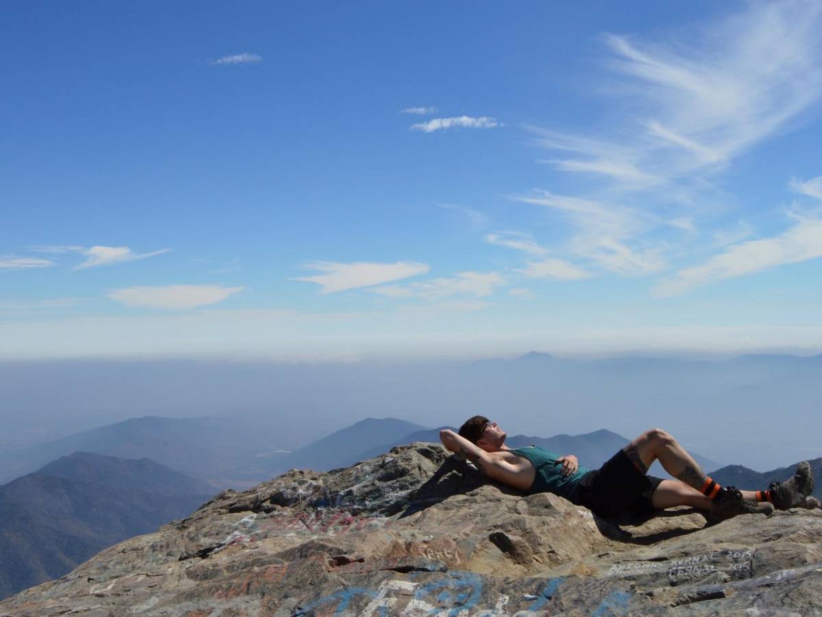 a student laying on a mountaintop in the Andes, surrounded by other mountains in the distance