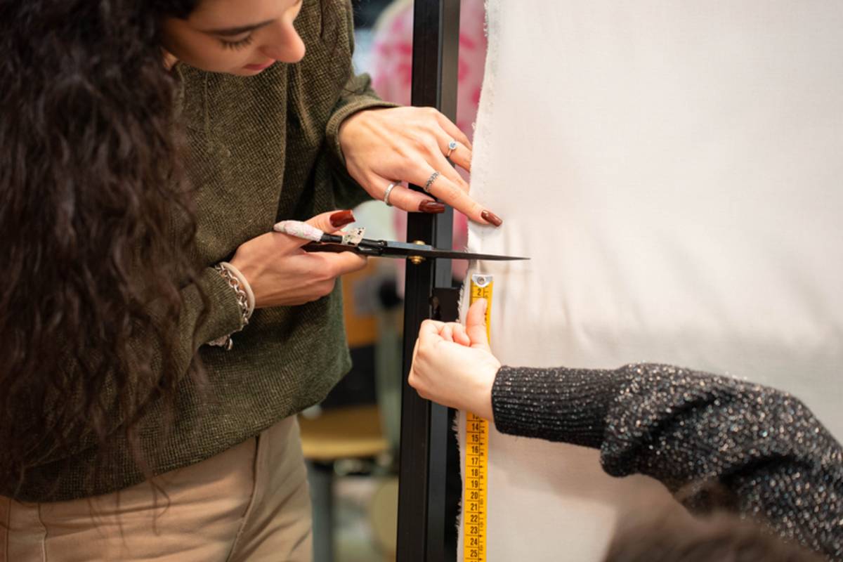 A student measuring and cutting some white fabric