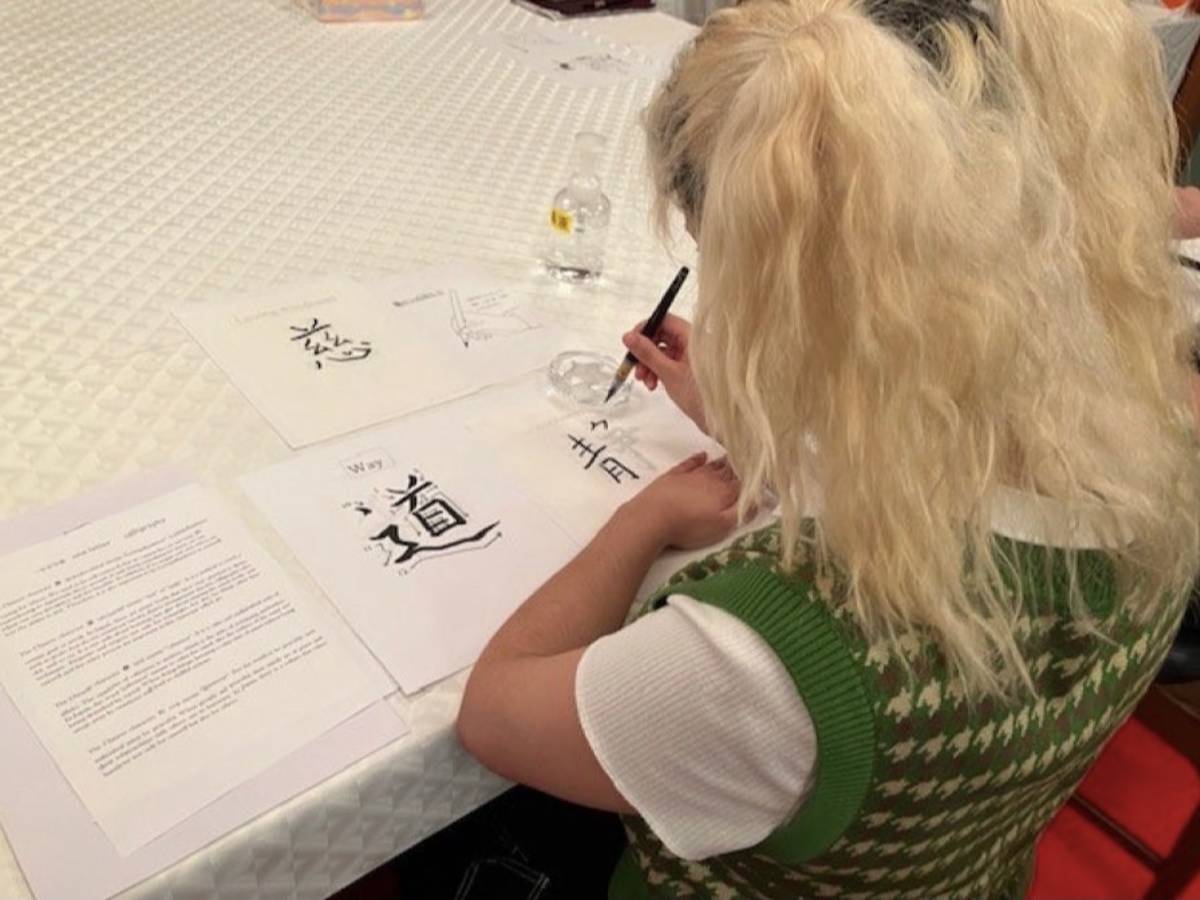 A student with long blonde hair at a table practicing Japanese calligraphy