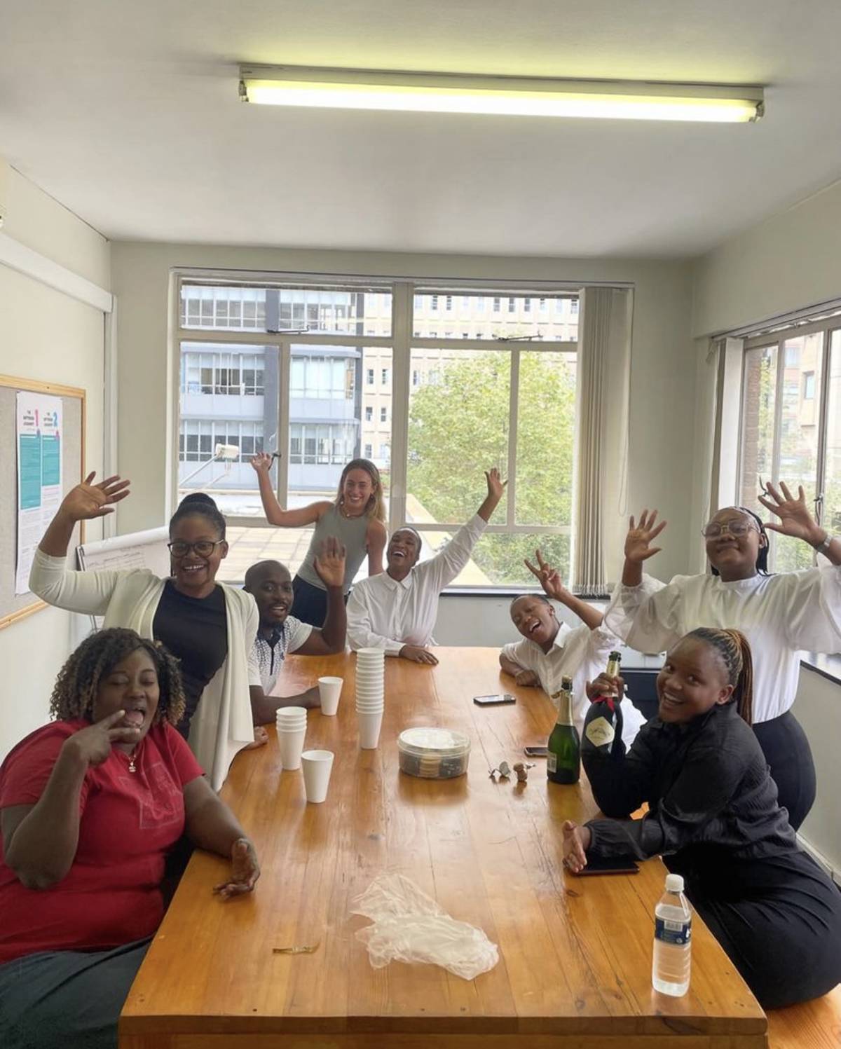 A volunteer and the team at the law clinic smile and wave at the camera, sat around a table celebrating with champagne!