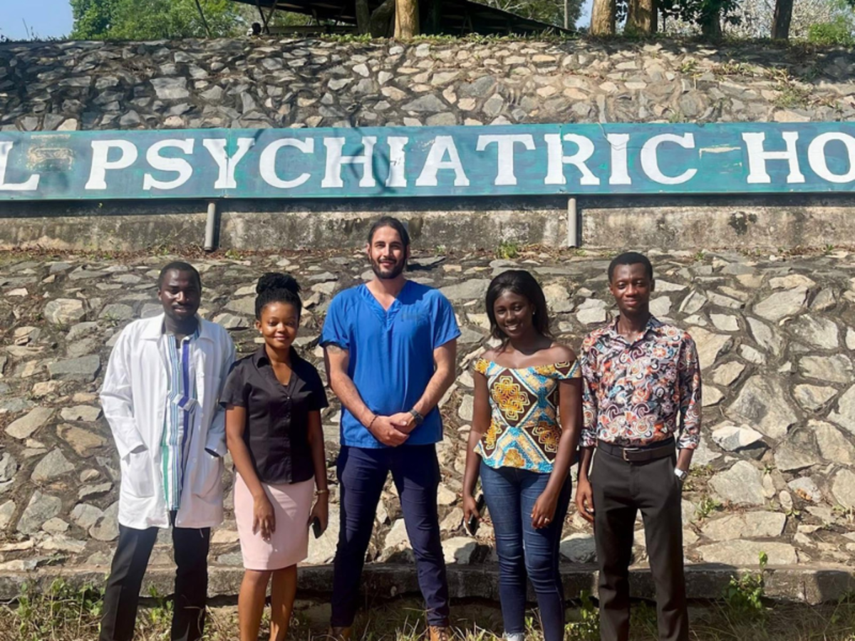 A volunteer poses in his scrubs outside a psychiatric hospital sign with members of the team.