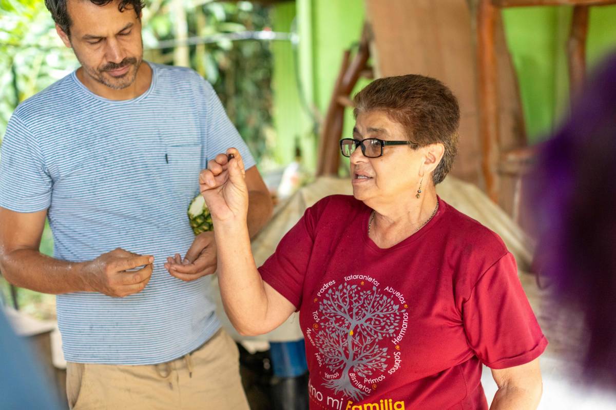 A woman holds up a single coffee bean, speaking to an audience out of view.
