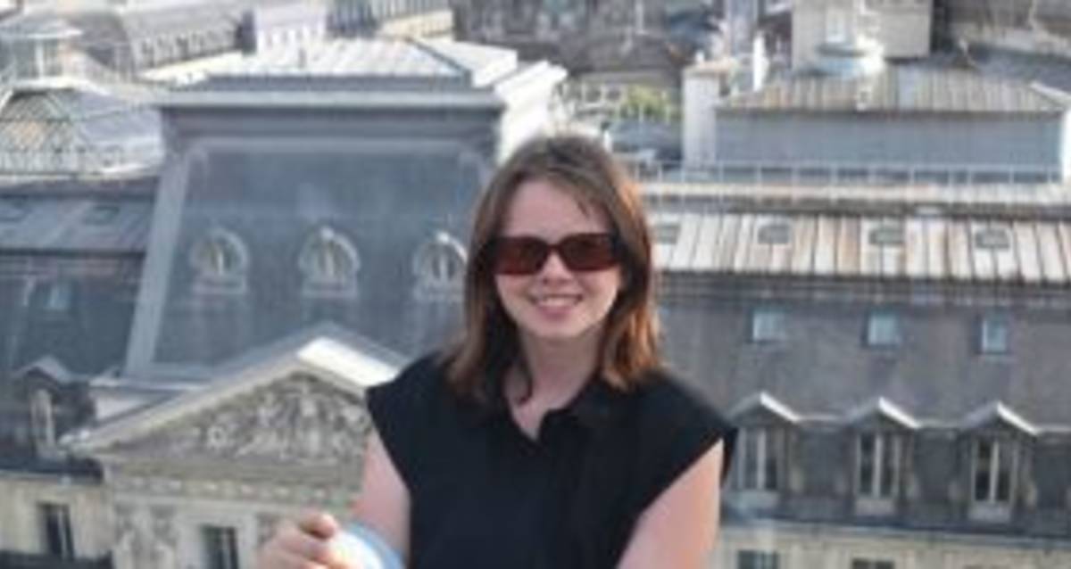 A woman in sunglasses sitting on a ledge, overlooking the city.