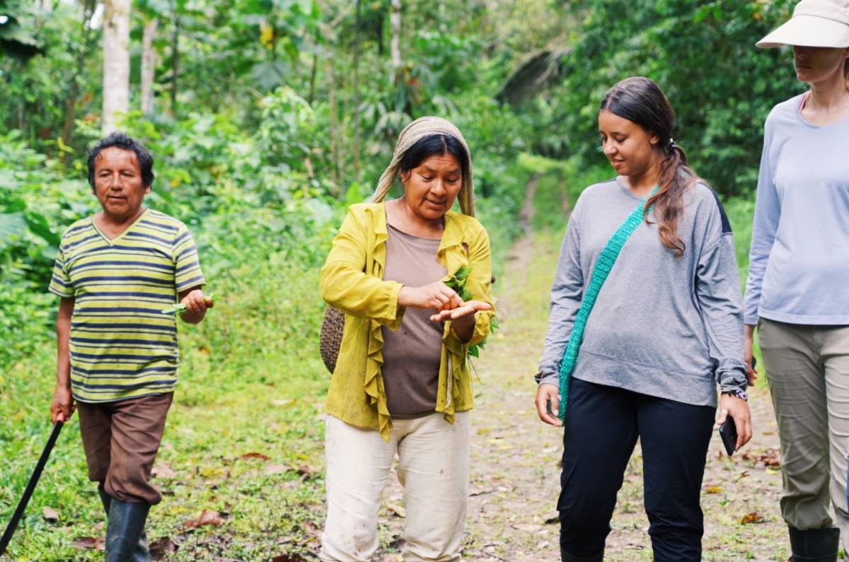 A woman indicates a plant she is holding, in conversation with a girl to her side. 