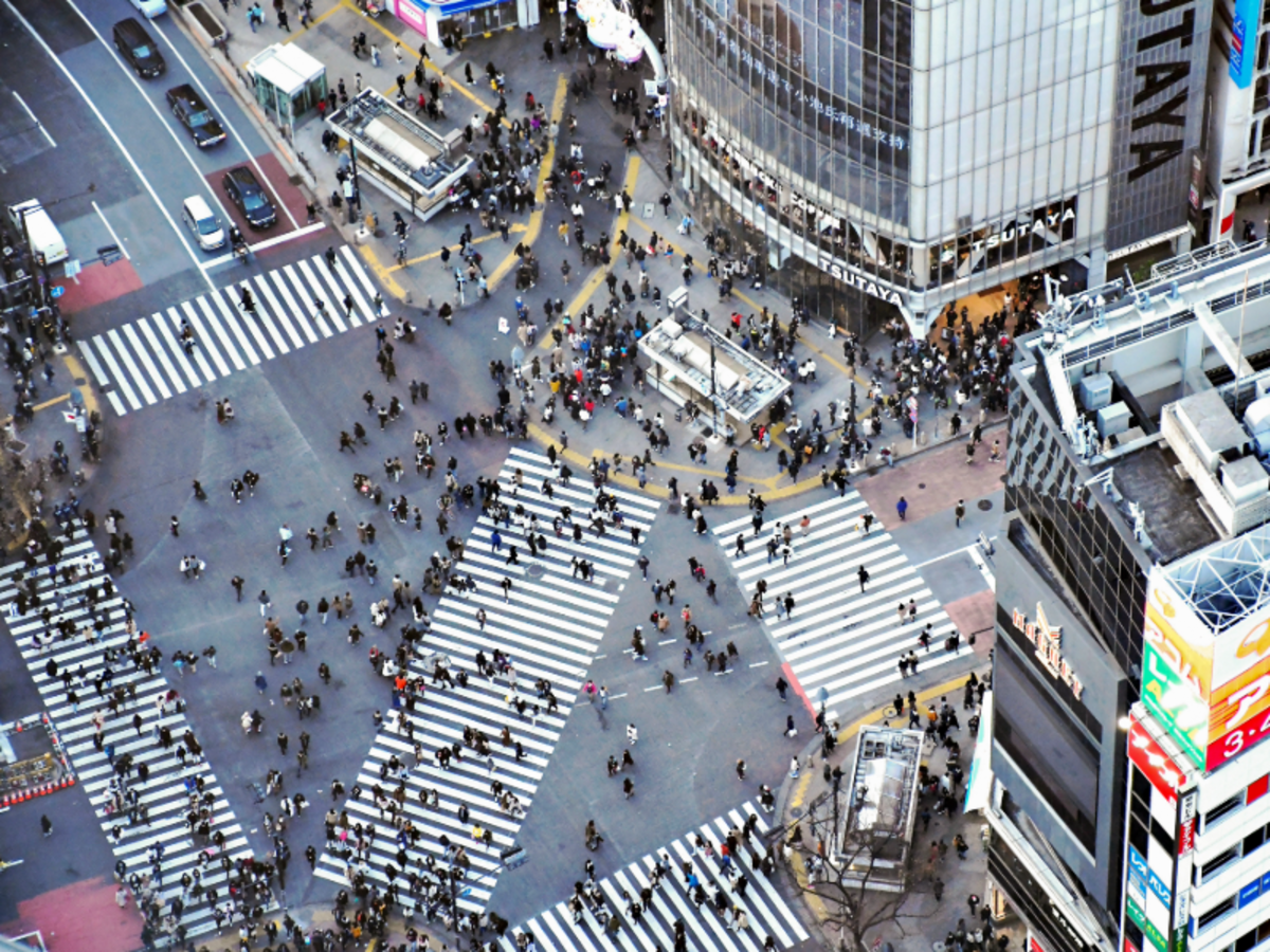 Aerial view of Shibuya Crossing in Tokyo with hundreds of pedestrians crossing from all directions among tall city buildings.
