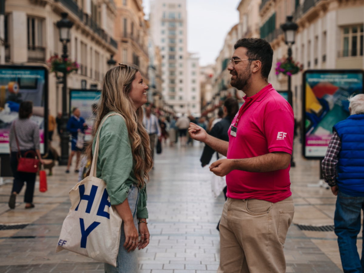 EF student and staff member talk on a busy shopping street in Malaga, surrounded by historic buildings and locals.