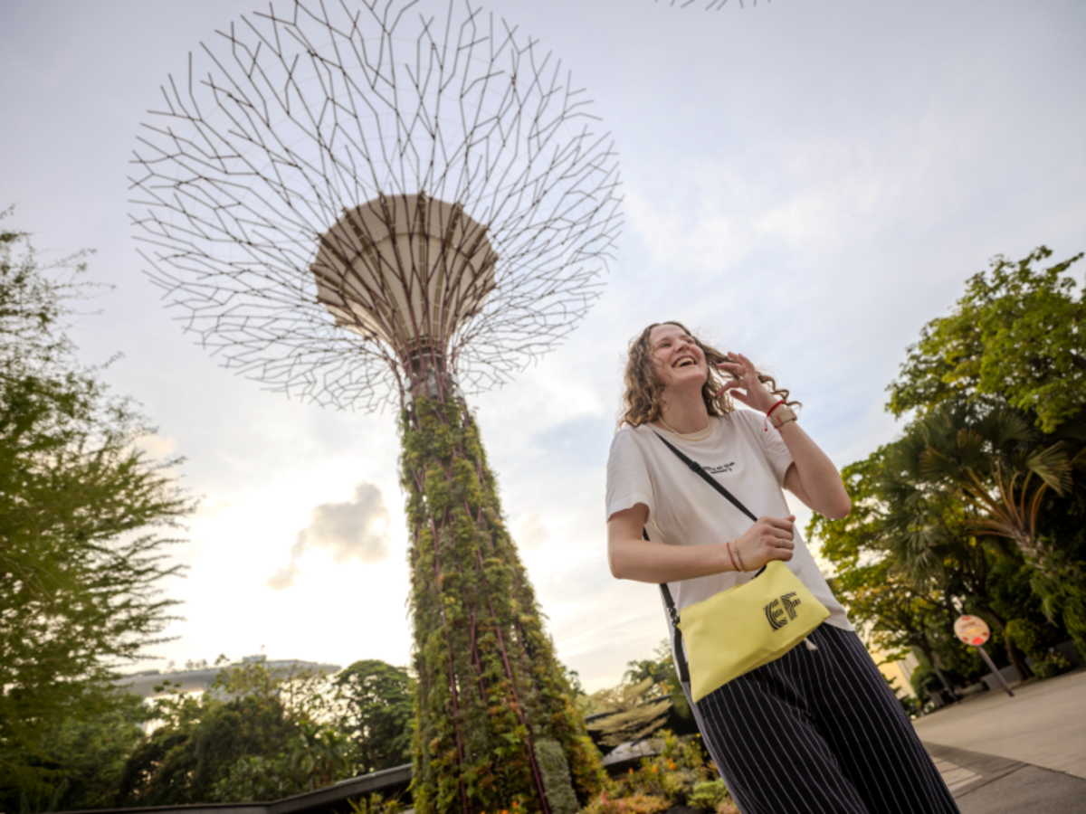 EF student smiling and walking at Gardens by the Bay in Singapore, with a Supertree towering behind.