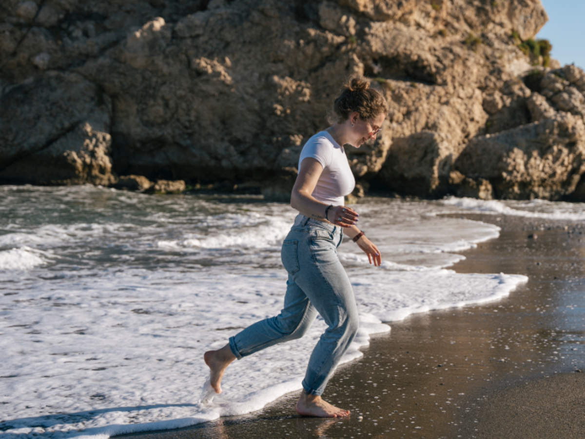 EF student walks barefoot along the shore in Malaga, enjoying the waves and rocky coastline.