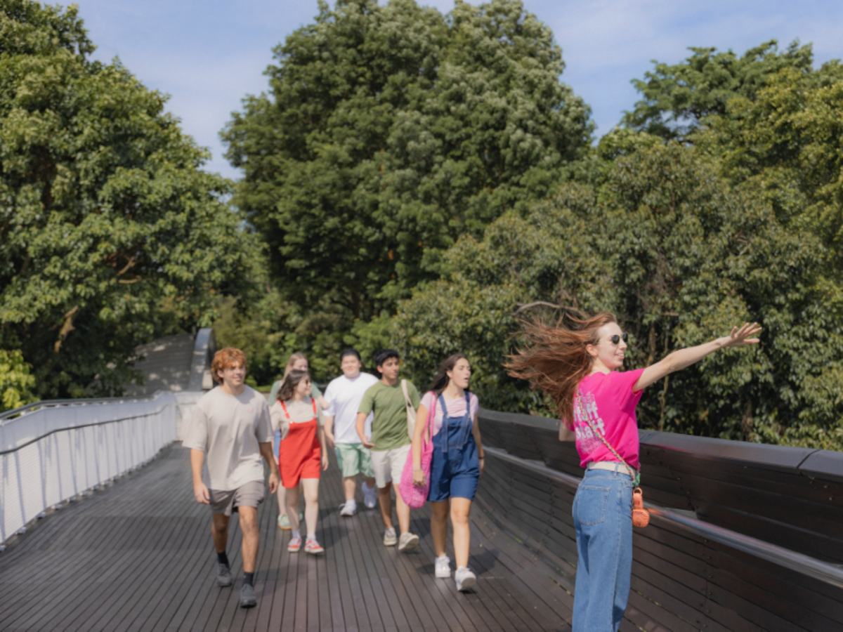 EF students walking with a staff leader across Henderson Waves bridge in Singapore, surrounded by lush greenery.