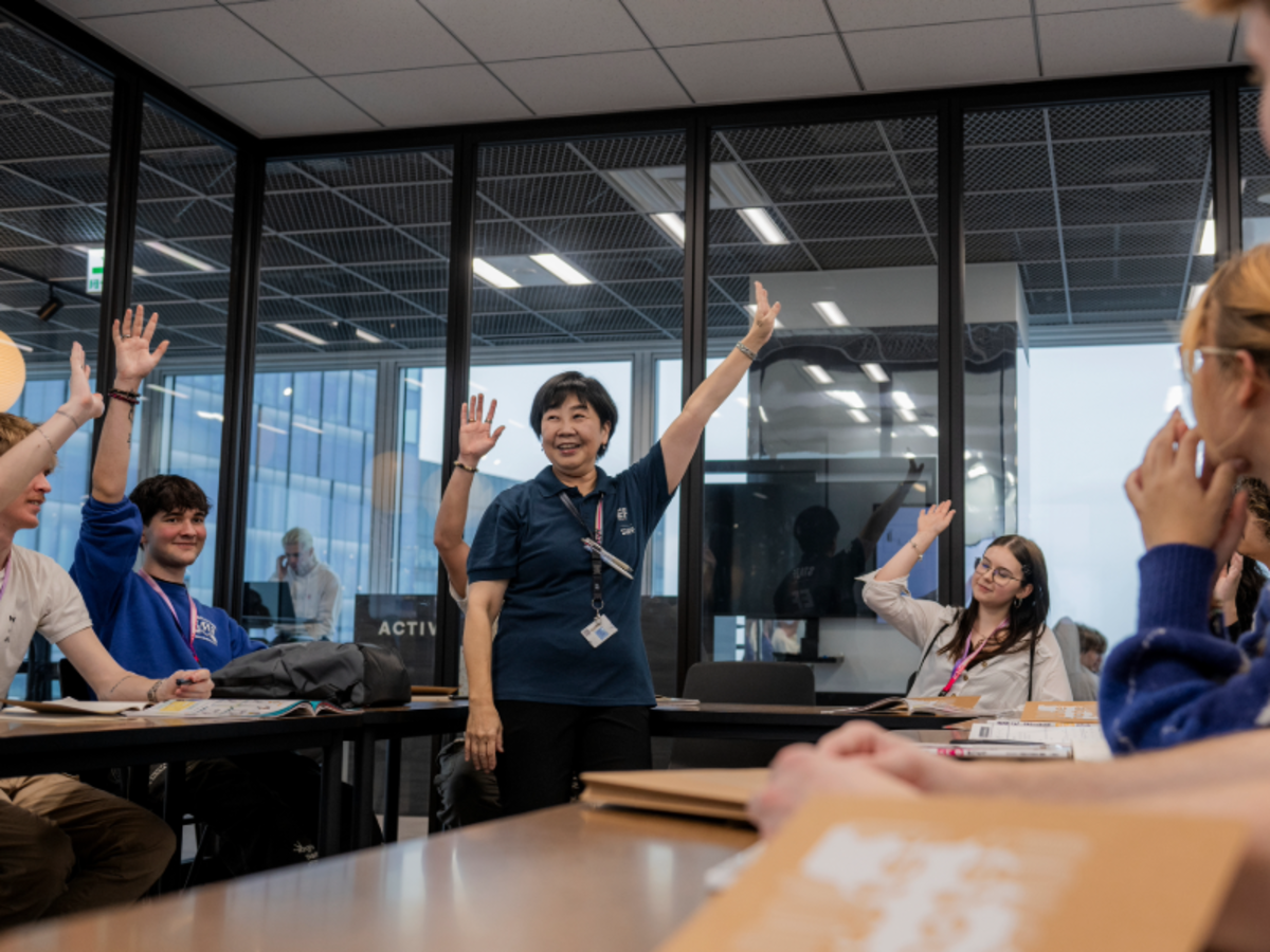 EF Tokyo students raise their hands in an interactive Japanese language class led by a smiling teacher.