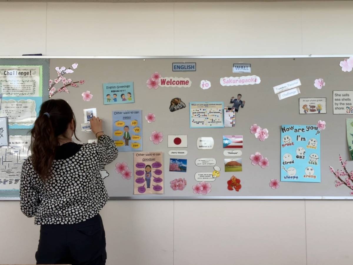 Female teacher rearranges resources on classroom display board.