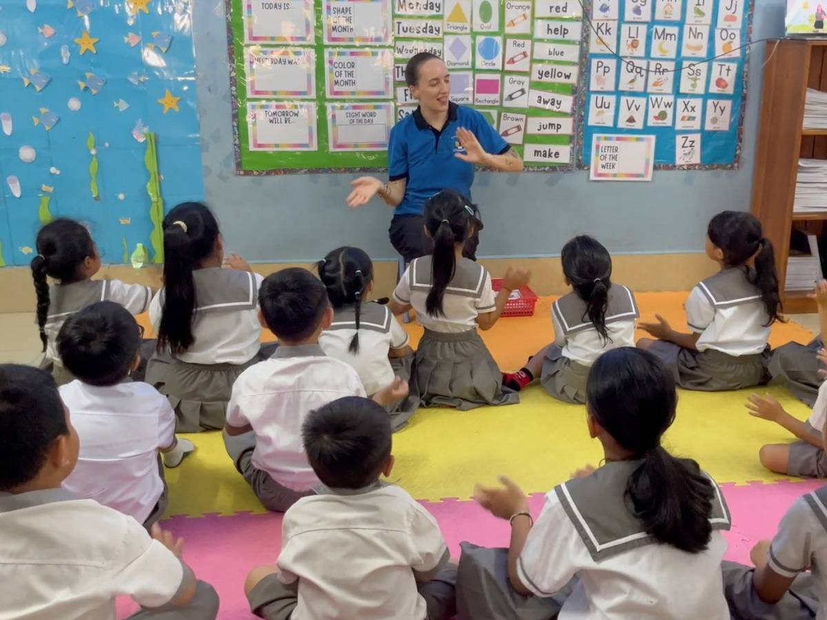 Female TEFL teacher leading a classroom of young students seated on the floor, using hand gestures during a lesson.