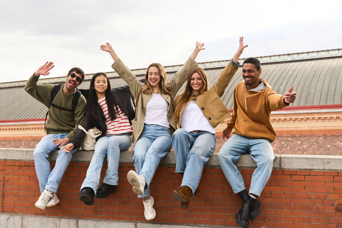 Five smiling friends cheering together on a brick ledge