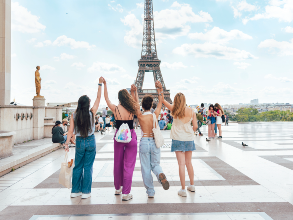 Four EF students holding hands with arms raised, facing the Eiffel Tower in Paris on a bright day.