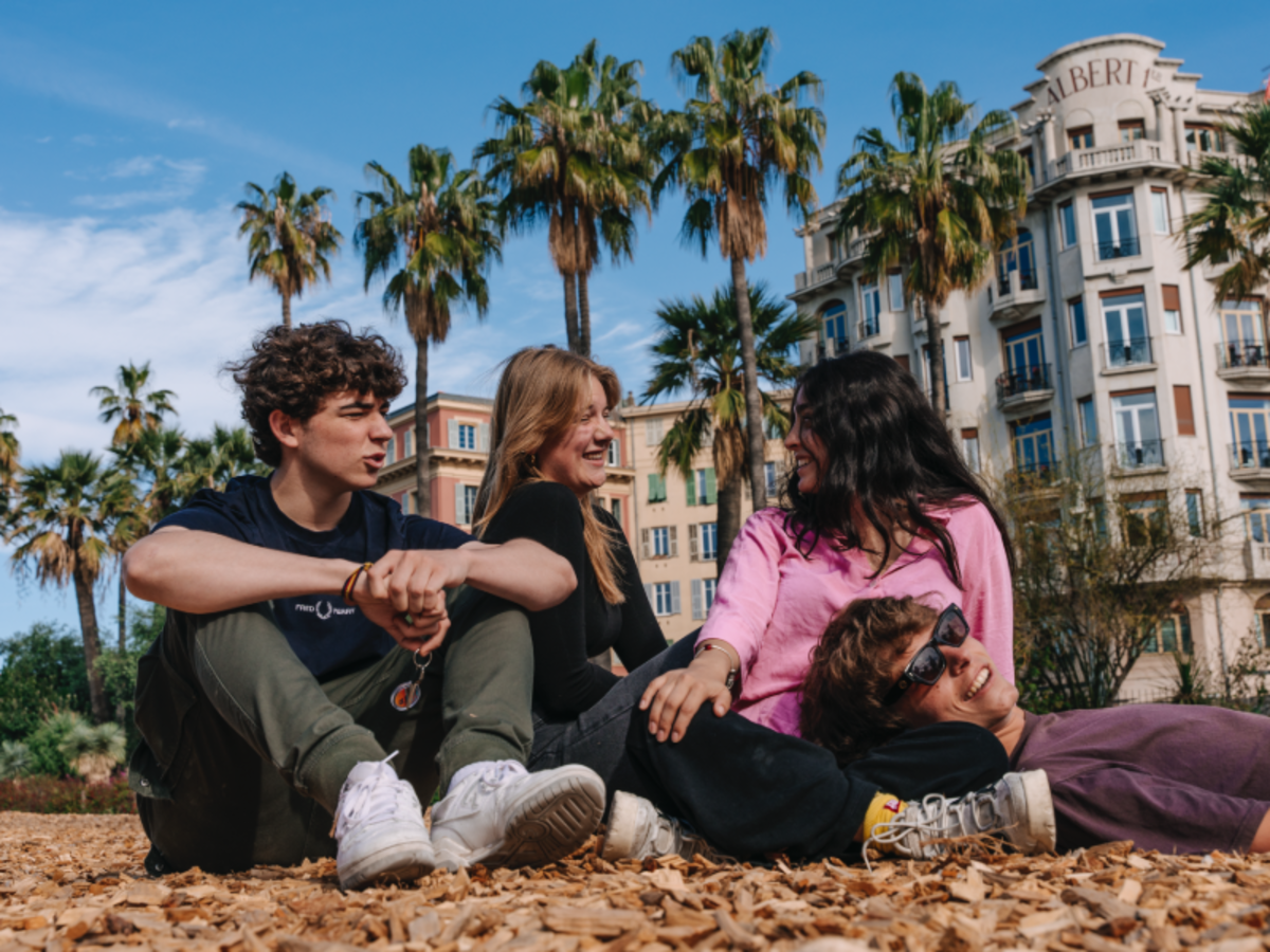 Four EF students relaxing outdoors on a sunny day, sitting under palm trees in a European city square.