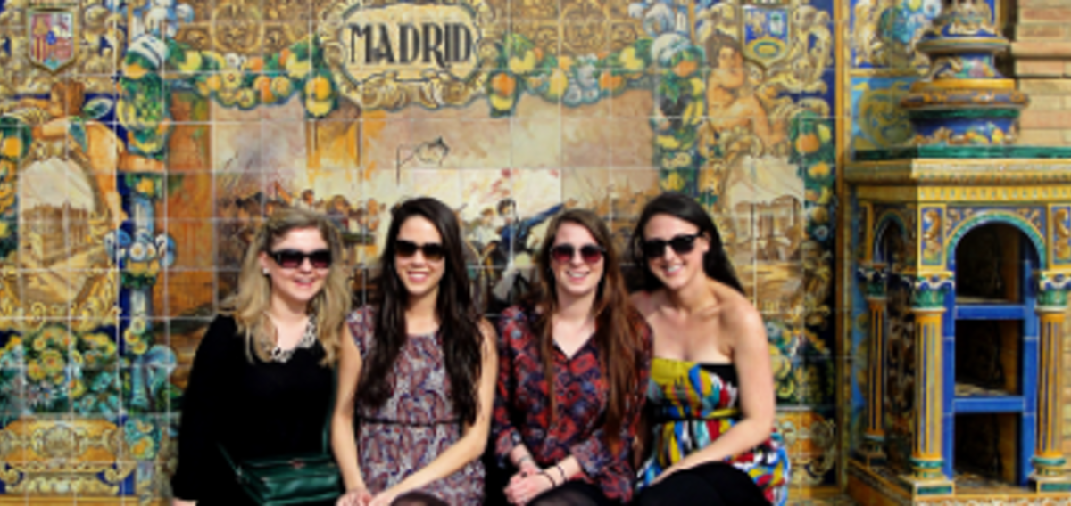 Four women sitting on a bench in front of a vibrant wall.