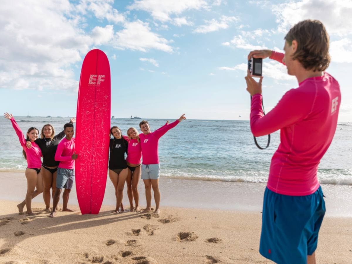 Group of EF Gap Year students on the beach in Tamarindo, Costa Rica posing with a bright pink surfboard while learning to surf as part of their study abroad program.