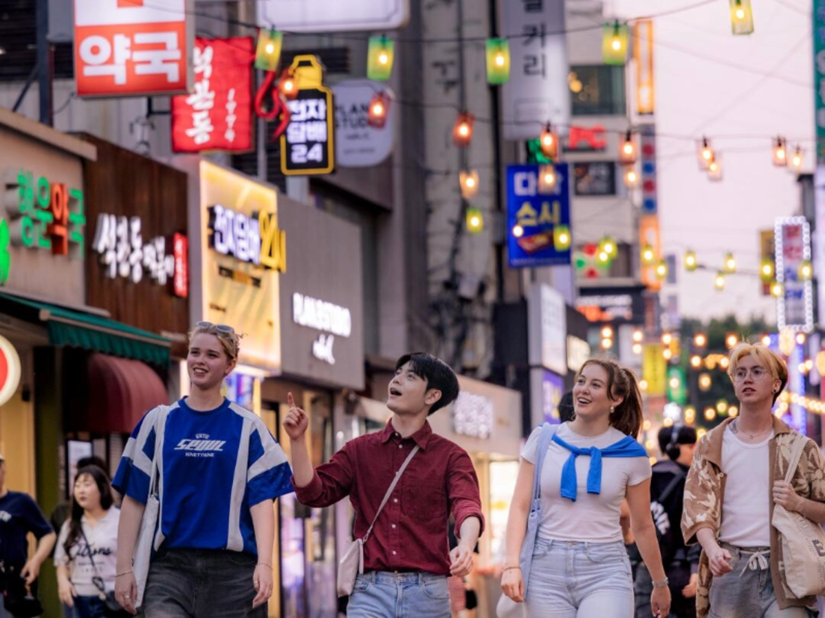 Group of EF Gap Year students walking through a bustling street in Seoul, South Korea at dusk, with colorful neon signs and hanging lanterns above.