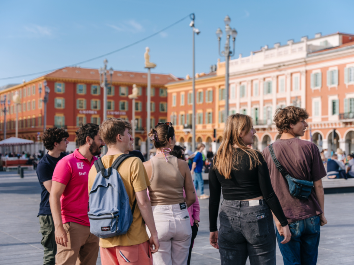Group of EF students exploring Place Masséna in Nice, surrounded by colorful historic buildings under a bright blue sky.