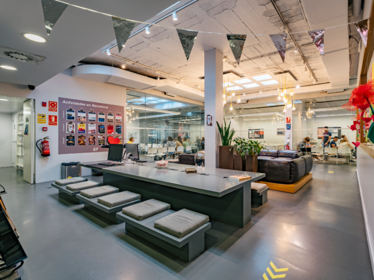 Interior of the EF Barcelona school, showing the reception area with study spaces and classrooms in the background.