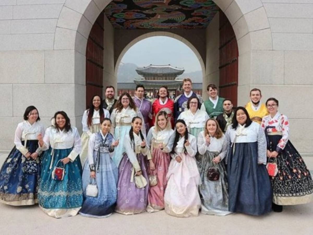 International teachers and students wearing traditional hanbok at a historic palace in South Korea.