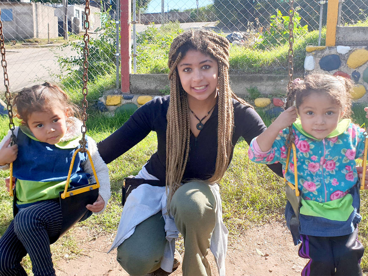 IVHQ Volunteer pushing two young children on a swing-set