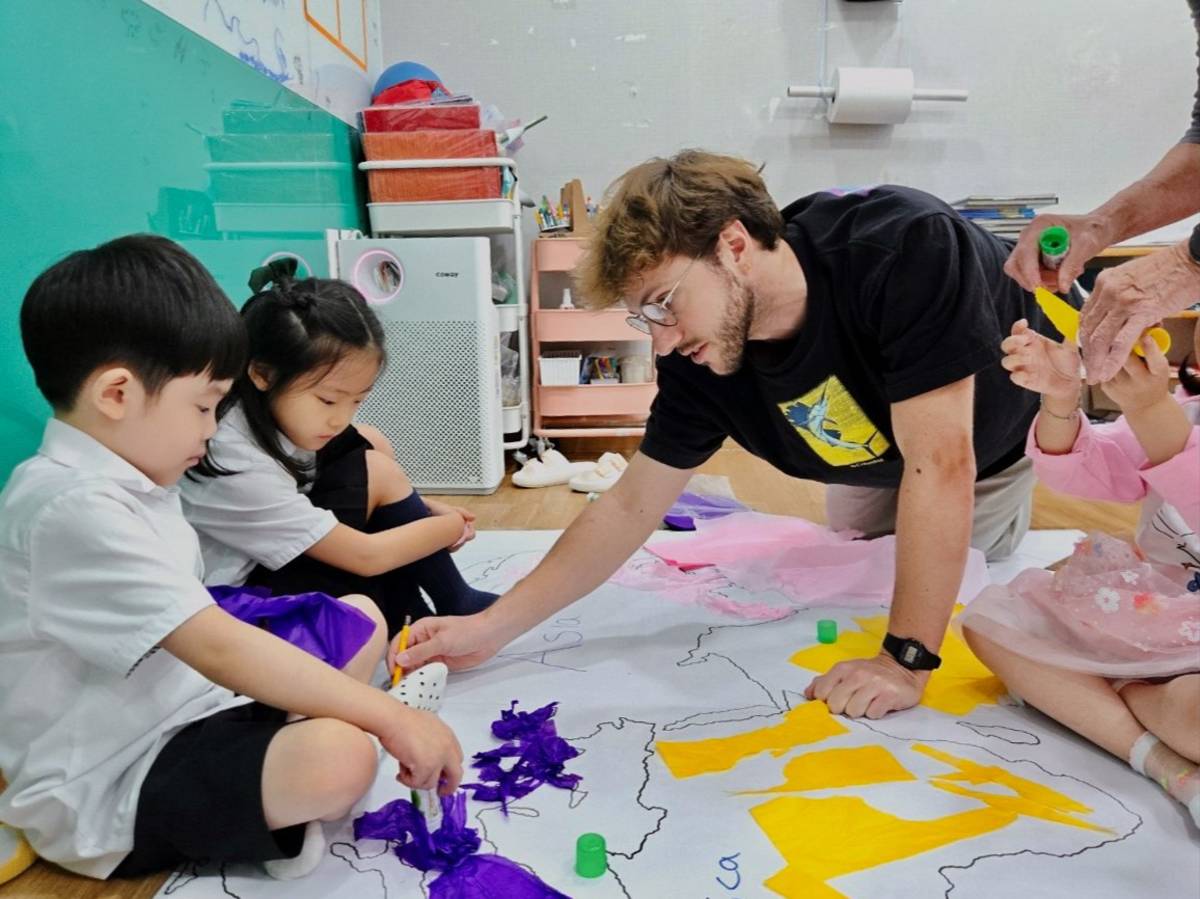 Male TEFL teacher kneeling on the floor, helping young students with their work.