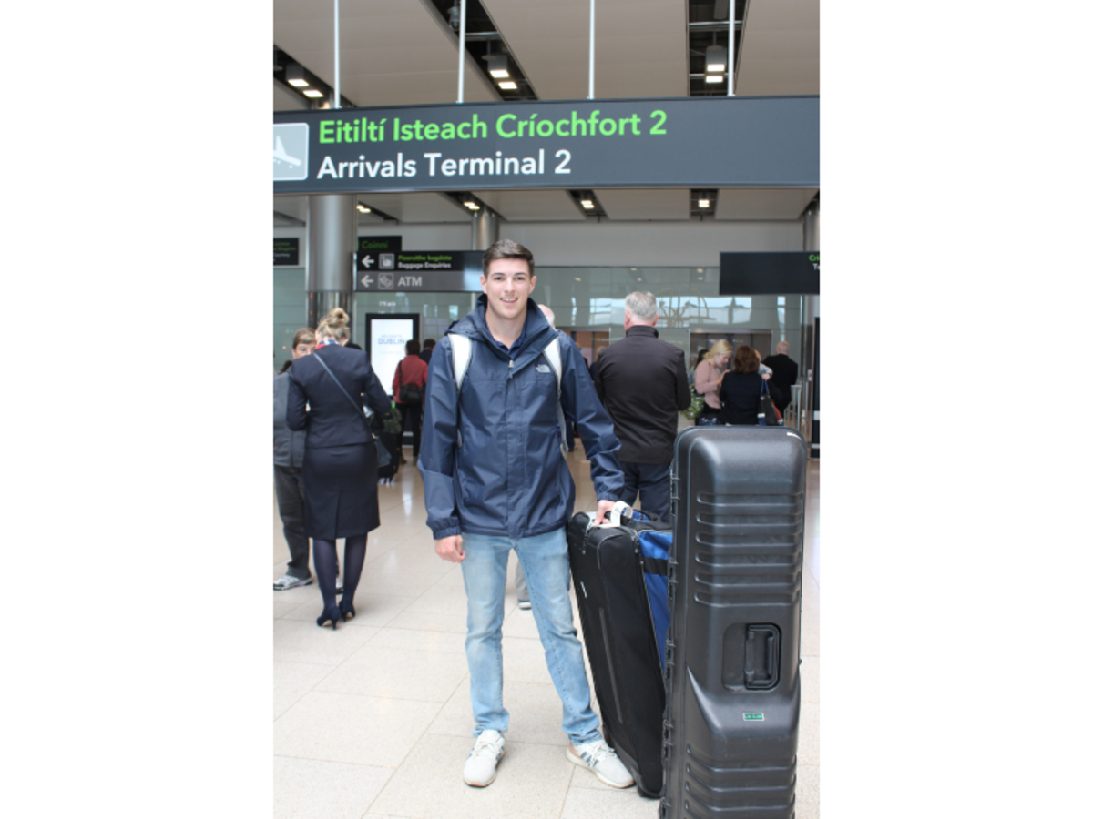 man smiling in an airport arrivals terminal with rolling luggage