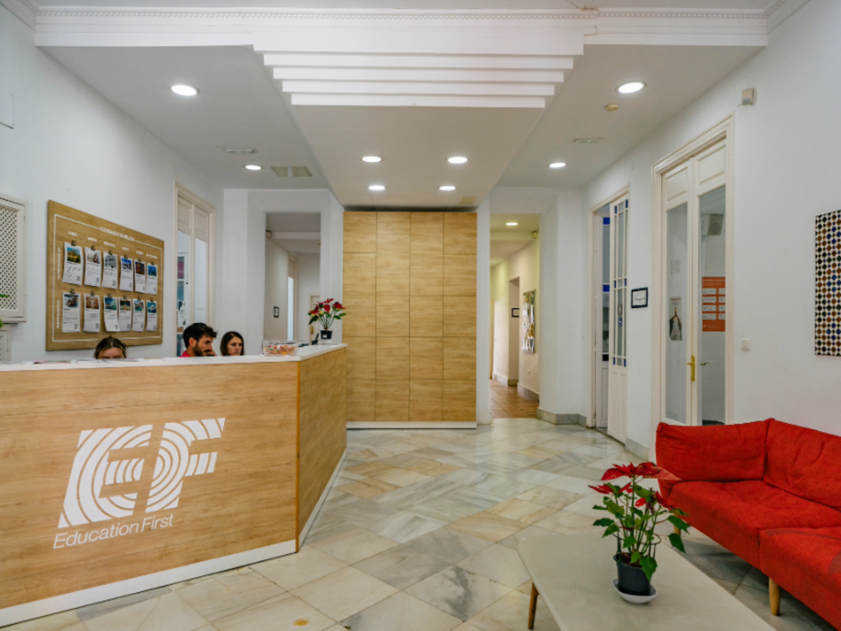 Modern reception area at EF Malaga language school with a wooden front desk, EF logo, red sofa, and welcoming staff.