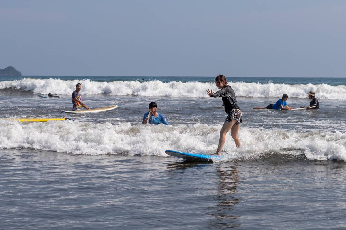 People surf in the waves, with a girl standing on board.