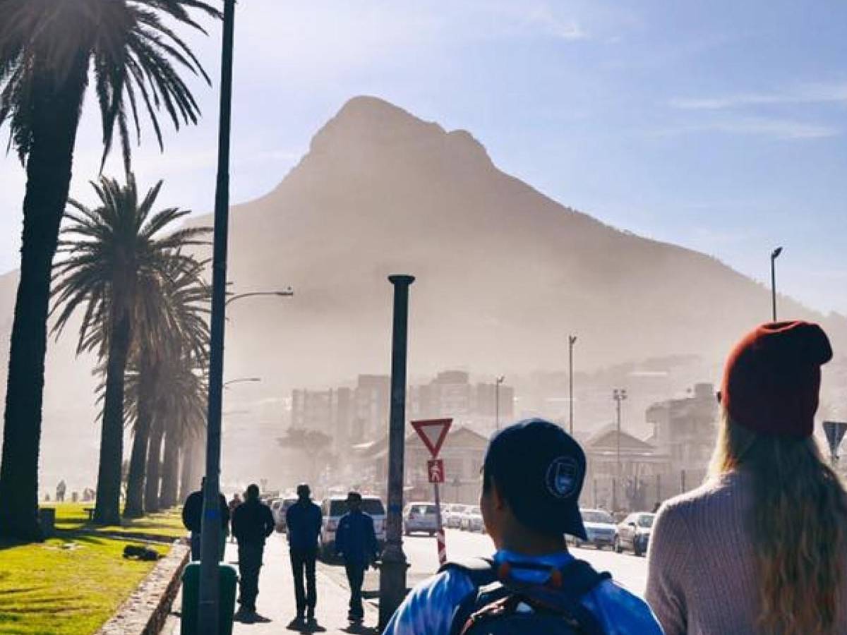People walk near the ocean with a view of a mountain in front of them in Cape Town