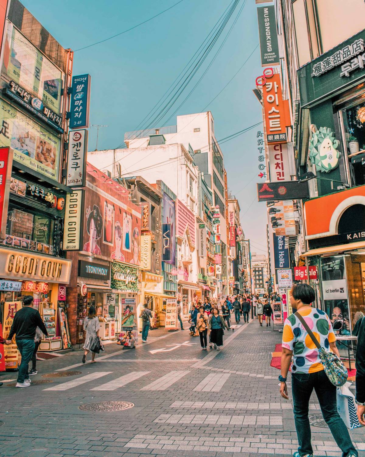 People walk on a paved street lined with colorful buildings and signs