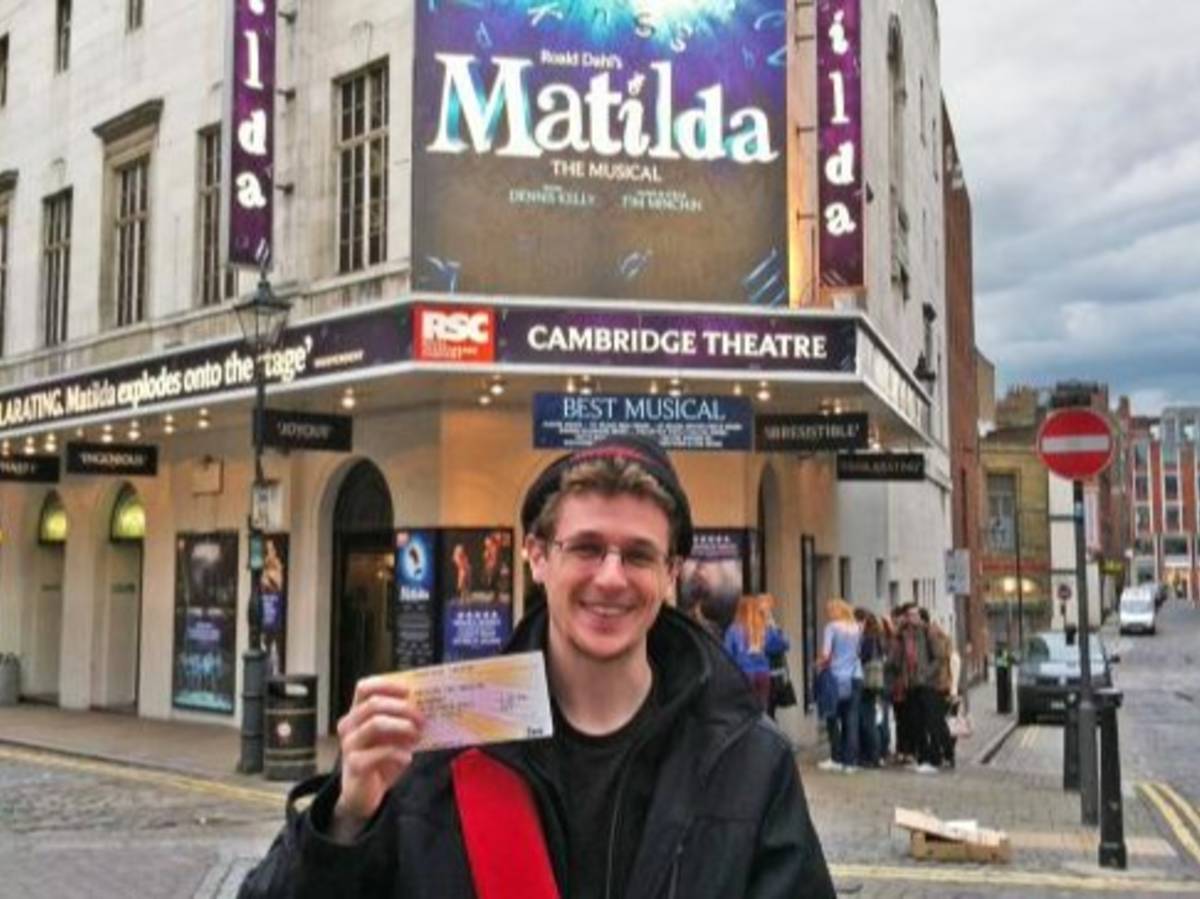 Person holding a theater ticket in front of the Cambridge Theatre in London, home of Matilda the Musical.