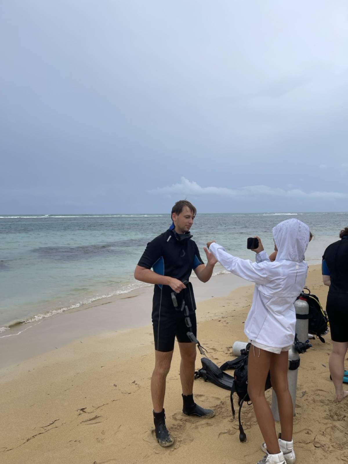 person in scuba gear with another person with camera on the beach